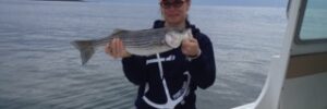 A woman holds up a striper fish she caught at Morning Flight Charters